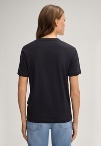 Schwarzes T-Shirt mit kurzen Ärmeln und Rundhalsausschnitt, glatte Textur und gerade geschnitten. Verfügt über ein kleines Logo-Label an der unteren Seite.