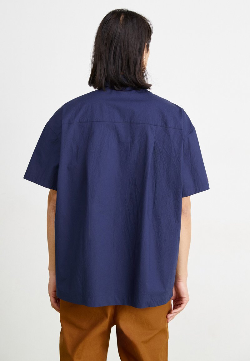 Chemise à manches courtes bleu marine avec une coupe décontractée, dotée d'une texture légèrement froissée et d'un ourlet droit, vue de dos.