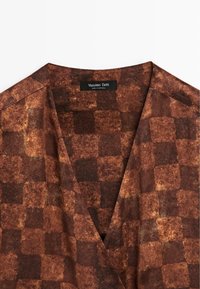 Hnědý károvaný oděv s výstřihem do V a texturovaným vzorem, uvnitř límce černá etiketa s nápisem "Massimo Dutti Made in Portugal".