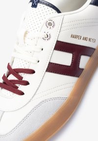 Zapatilla blanca con acentos en color burdeos, ojales de encaje texturizados y suela de goma. Presenta el nombre de la marca "HARPER AND NEYER" en dorado en el lateral.