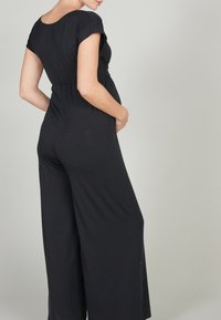 Combinaison noire avec un corsage ajusté et une coupe évasée. Elle présente des manches courtes et un tissu doux et extensible avec une texture subtile.