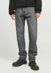 Inimene, kes kannab halli lõdva lõikega pükse, musti pits-up kingi ja musta tekstuuriga pika varrukaga pusa, taustaks hele ühtlane pind.