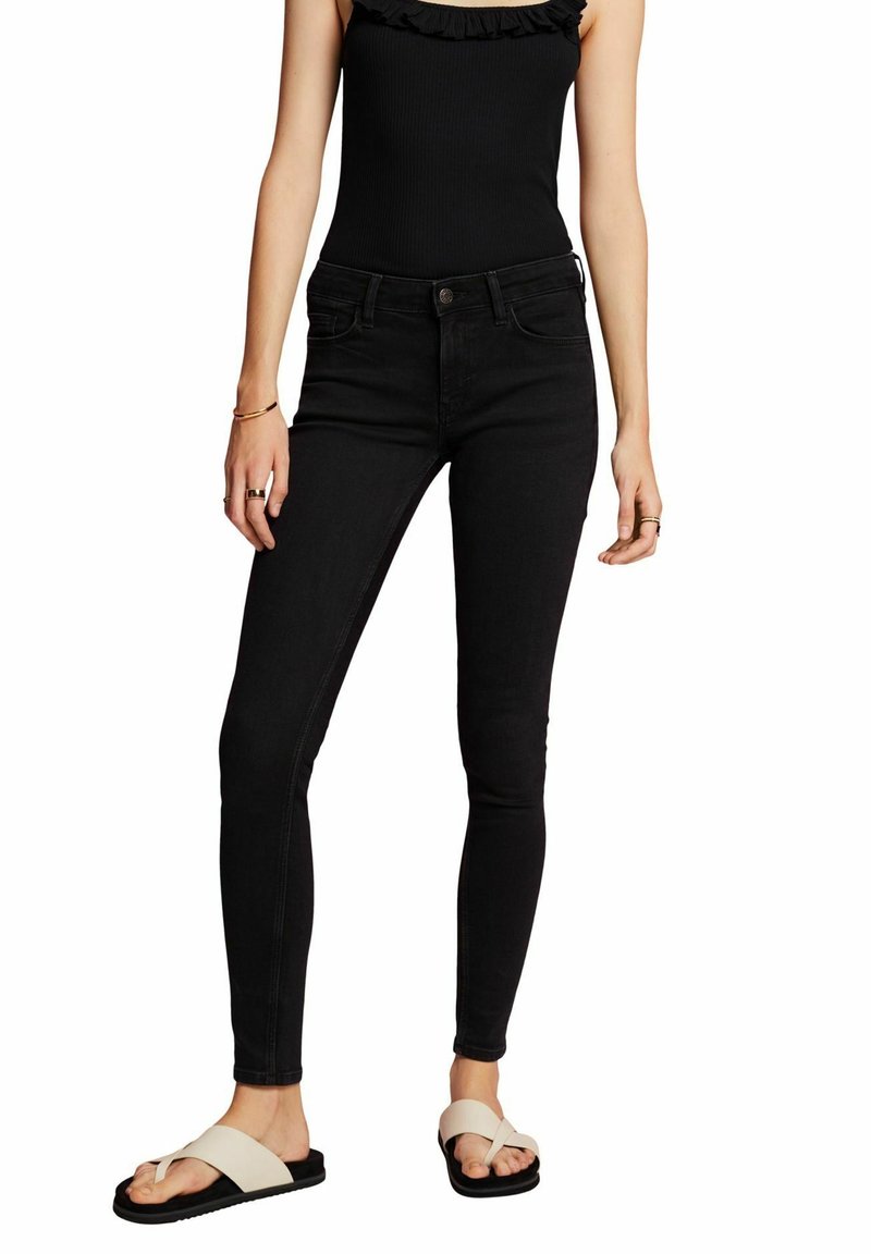 Jeans skinny negros de mezclilla con un diseño limpio. Combinados con chanclas beige, presentando un look casual.