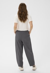 Pantalon gris à jambes larges avec une texture lisse, taille élastique et poches latérales, associé à un haut blanc à manches courtes et des chaussures décontractées.