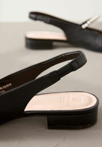 Mustat slingback-sandaalit, joissa on matala block-korkeus. Valmistettu sileästä nahasta, jossa on teksturoitu hihna ja pehmeä, vaaleanvärinen pohja.