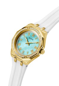 Gold-toned octagonal watch with a turquoise dial, Roman numerals, and crystal accents. Features a white silicone strap.