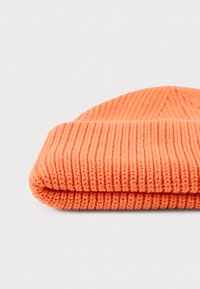 Oranssi neulottu pipo, jossa on ribbikyky ja kääntöpanta. Materiaali näyttää pehmeältä ja paksulta, sopivalta kylmään säähän.