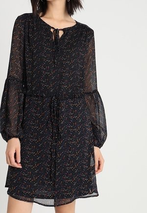 Musta kukkakuvioinen mekko, jossa on pitkät, pöyhistetyt hihat, solmittava kaula-aukko ja vyötärö. Kangas on kevyt ja puoliläpinäkyvä, monivärinen kuvio.