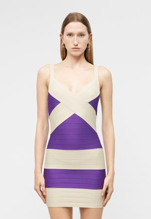 Γυναίκα που στέκεται με το σώμα προς τα εμπρός, φορώντας ένα μωβ και μπεζ εφαρμοστό φόρεμα χωρίς μανίκια με οριζόντιες και διασταυρωμένες ρίγες.