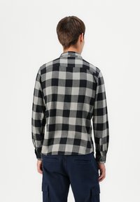 Camisa de cuadros en negro y gris, de manga larga y fabricada con tejido suave, con cuello abotonado y puños estructurados, vista desde la parte de atrás.