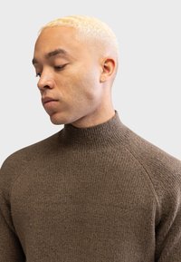 Brown ribbed turtleneck sweater with a fitted design and raglan sleeves. Made from a soft, textured material.
