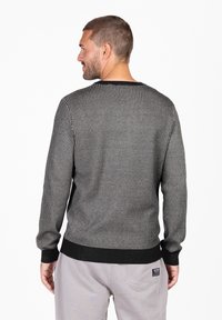 Sweter dziany w czarno-białym wzorze w psa zębatego, z długimi rękawami, okrągłym dekoltem, ściągaczami przy mankietach i dole, wykonany z miękkiego materiału.