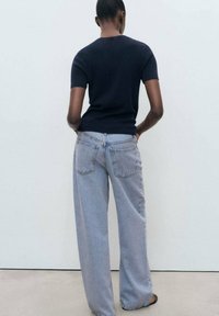 Marinblå kortärmad figurnära topp kombinerad med ljusblå högmidjade vida jeans, med bakfickor och en avslappnad silhuett.