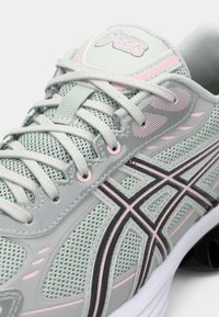 Chaussure de course Asics gris clair et rose avec tissu en mesh et lacets croisés, affichant le logo de la marque sur la languette et le côté.