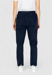 Pantaloni blu navy con vita elastica e vestibilità rilassata, dotati di due tasche posteriori e orli con risvolto. Realizzati in un tessuto morbido.