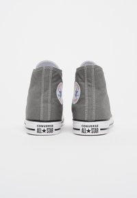 Grijze canvas hoge sneakers met witte rubberen zolen, voorzien van zwarte streepaccenten en ronde logo-patches aan de zijkanten.