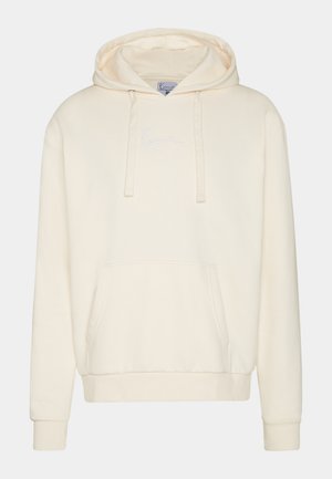 Krēmo krāsas kapuce ar auklām, kabatu priekšpusē un ribinātām piedurknēm un apakšmalu. Uz krūtīm ir smalki izšūts balts logo.