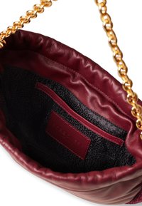 Innenteil einer kastanienbraunen, ledernen Handtasche mit einer gesteppten Textur, ausgestattet mit einem schwarzen, gemusterten Futter und einer kleinen Innentasche. Sichtbarer goldfarbener Kettenriemen.
