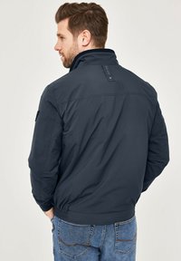 Dark navy bomber jacket made of smooth fabric, featuring a high collar, elastic cuffs, side pockets, and a textured back detail.