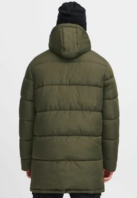 Zimska parka u maslinasto zelenoj boji s kapuljačom, koja ima horizontalno qulitanje i malo duži kroj za bolju pokrivenost. Izrađena je od glatkog materijala.