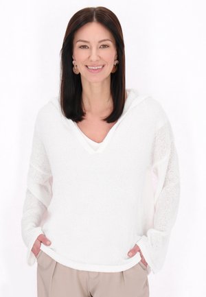 Felpa bianca a maglia con scollo a V, vestibilità ampia e maniche lunghe. Presenta un motivo testurizzato e un tessuto morbido e leggero. Abbinata a pantaloni beige.