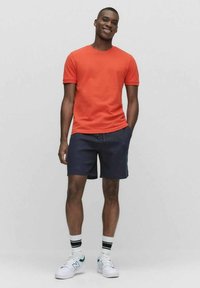 Röd kortärmad t-shirt, marinblå shorts, vita sneakers med gröna detaljer och randiga strumpor. Slät tyg, avslappnad passform och avslappnad stil.