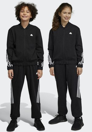 Tute sportivi neri con strisce bianche su maniche e pantaloni. Il materiale è liscio, con polsini elasticizzati e design aderente.