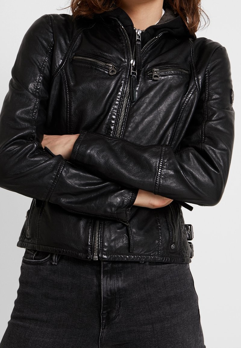 Veste en cuir noir avec fermeture éclair sur le devant, plusieurs poches zippées, détails matelassés et boucles latérales ajustables. Texture lisse.