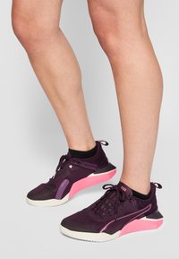 Lila Sport Schuhe mit einem Obermaterial aus Mesh, pinken Akzenten und schwarzer Gummisohle. Sie zeichnen sich durch ein niedriges Profil und Schnürsenkel für einen sicheren Halt aus.