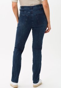 Jeans en denim bleu foncé à coupe slim, taille haute, deux poches arrière et détails de couture subtils. Tissu léger avec légèrement d'élasticité.