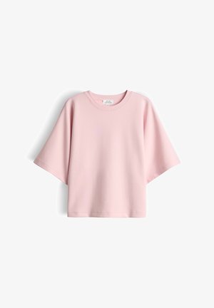 Lichtroze oversized shirt met korte mouwen en een ronde hals, met een rechte zoom, platliggend op een witte achtergrond.