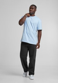 Ljusblå, kortärmad t-shirt med vita vertikala ränder, ihop med mörkgrå byxor och vita sneakers. Enkel rund halsringning, avslappnad passform.