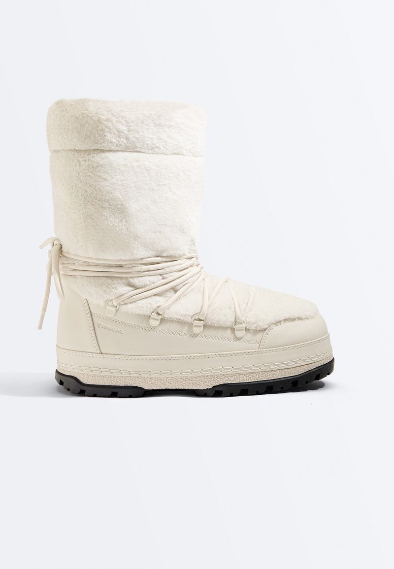 Botte d’hiver blanche haute avec dessus en polaire douce, fermeture à lacets devant, semelle épaisse et semelle extérieure texturée noire pour une bonne accroche.