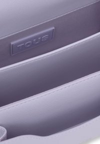 Light purple leather handbag interior featuring divided compartments and a smooth texture. Includes a raised "TOUS" logo label.
