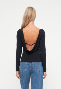 Czarny top z długim rękawem, z głębokim dekoltem z tyłu, z paskiem i miękką fakturą, w połączeniu z jasnoniebieskimi spodniami o wysokim stanie.