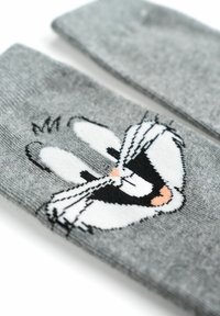 Calzini grigi con un design di personaggio dei cartoni animati raffigurante una faccia sorridente con occhi prominenti, dettagli in bianco e nero e un accento rosa sul naso.