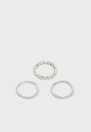 Trois bagues en argent avec de petites pierres précieuses claires réparties uniformément autour des anneaux sur un fond clair uni.