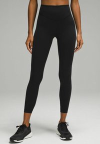 Black high-waisted leggings with a smooth texture and fitted design, paired with black athletic shoes featuring a white sole.