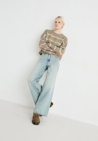 Suéter de punto beige con rayas onduladas en rosa y crema, combinado con jeans de pierna ancha de color azul claro y zapatos marrones con cordones.