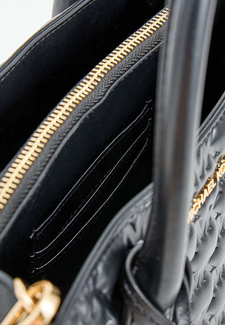 Intérieur d'un sac à main en cuir noir avec une fermeture éclair dorée, plusieurs emplacements pour cartes et un motif texturé. Dispose de deux anses pour un transport facile.