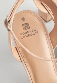 Sandale à talon haut en daim nude avec un talon carré, une sangle de cheville réglable et un logo "Forever Comfort®" en relief sur la semelle intérieure.