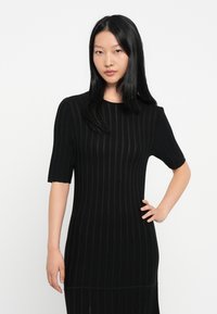 Crna rebrasta haljina s kratkim rukavima i prilagođenim siluetom. Sadrži vertikalne pruge za teksturu i okrugli izrez.