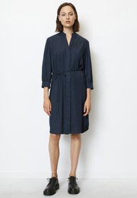 Abito camicia blu navy con colletto, maniche a tre quarti, cintura in vita e una texture liscia. Abbinato a scarpe nere stringate.