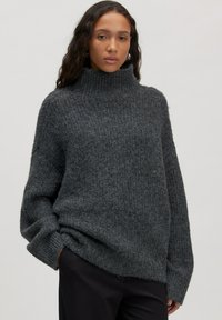 Chunky grijze coltrui met geribbelde textuur, oversized pasvorm en verlaagde schouders. Zacht, dik materiaal zorgt voor een gezellige uitstraling.