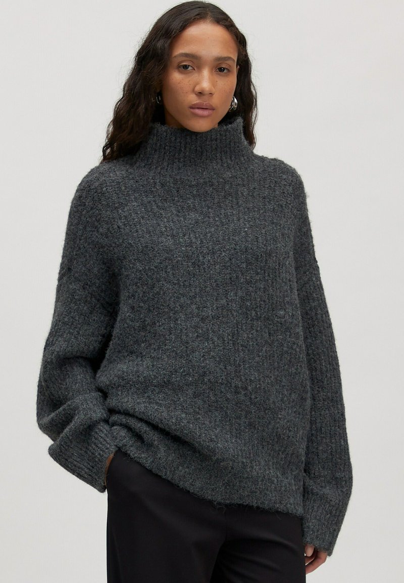 Chunky grijze coltrui met geribbelde textuur, oversized pasvorm en verlaagde schouders. Zacht, dik materiaal zorgt voor een gezellige uitstraling.