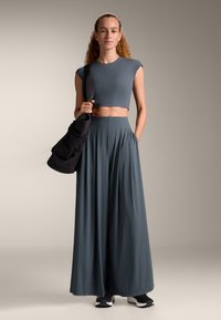 Gray cropped top and long, flowy gray skirt, made of smooth fabric, with a relaxed silhouette and pockets, paired with black shoes and bag.