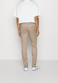 Beiga bomullbyxor med smal passform, med bakfickor och en slät yta, tillsammans med en enfärgad vit t-shirt och vita sneakers.