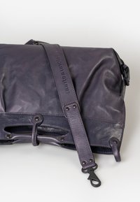 Borsa in pelle viola con una texture liscia, caratterizzata da una cintura decorativa, accessori in metallo e dettagli intagliati lungo i bordi.