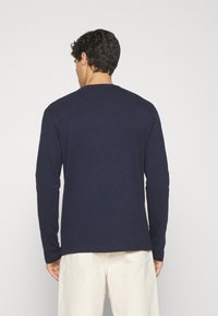 Chemise à manches longues bleue en coton doux, avec un col rond, des lignes épurées et une coupe décontractée, associée à un pantalon de couleur claire.