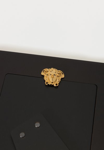 Rama foto neagră cu un emblemă a capului Medusa aurit centrată pe marginea superioară pe un fundal alb.